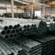 Close em estoque de tubos de aço galvanizado redondos e tubos de aço carbono quadrados organizados em prateleiras industriais dentro de um galpão logístico.